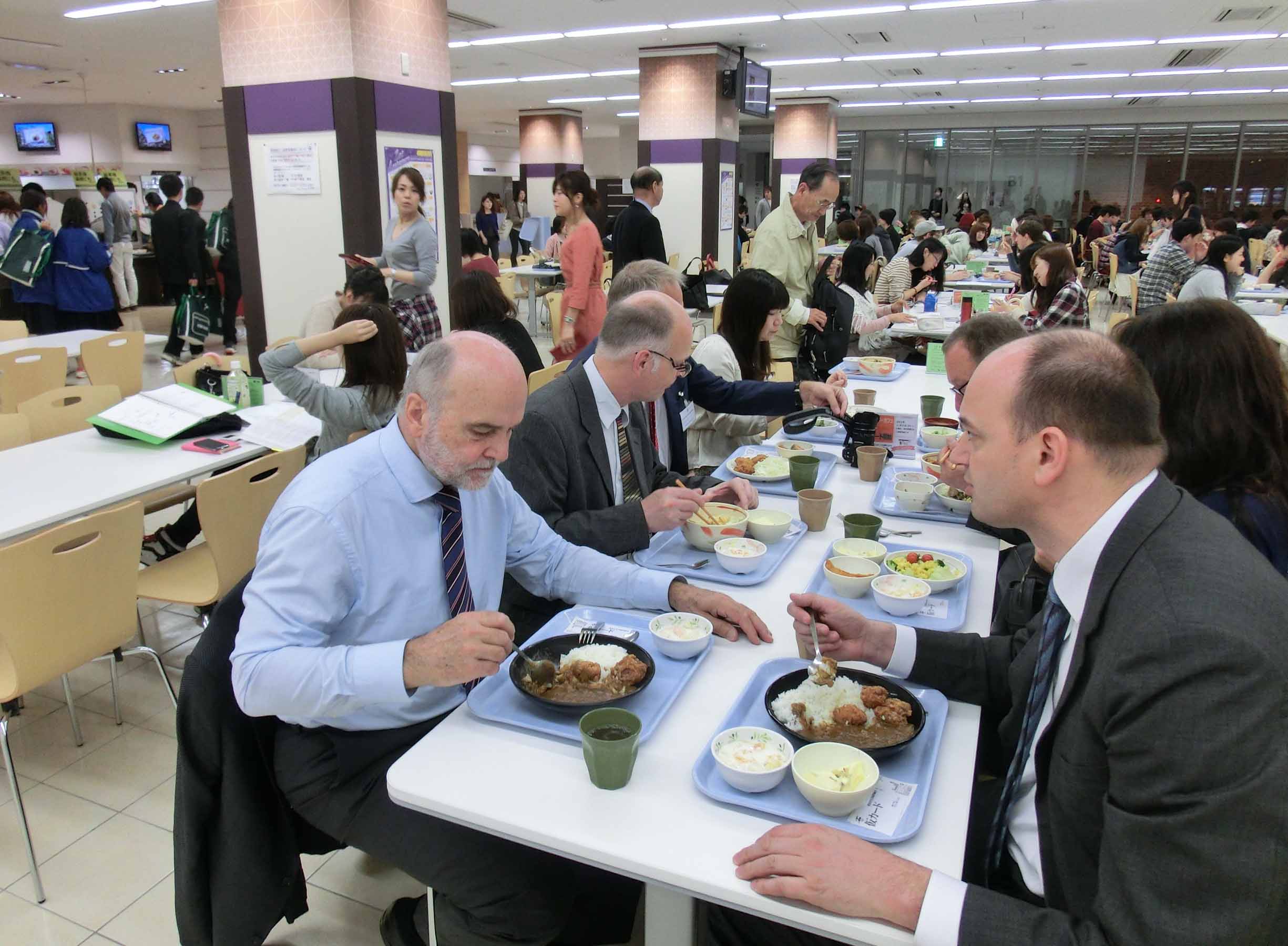Fünf Personen aus einer Delegation, die in einer japanischen Mensa zu mittag essen: Ein großer Raum, mit vielen Tischen in langen Reihen. Alle haben ein Tablett vor sich stehen