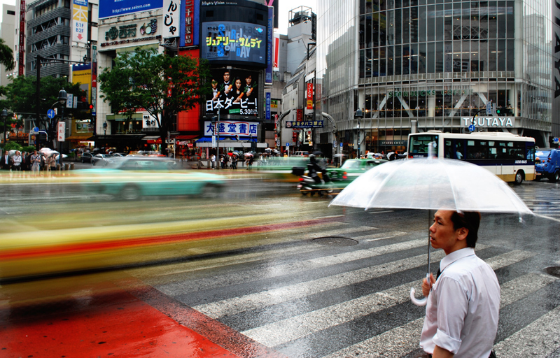 Fotomotiv aus der Ausstellung "Perspektive Asiens": Mann mit Regenschirm an einer vielbefahrenen Straße