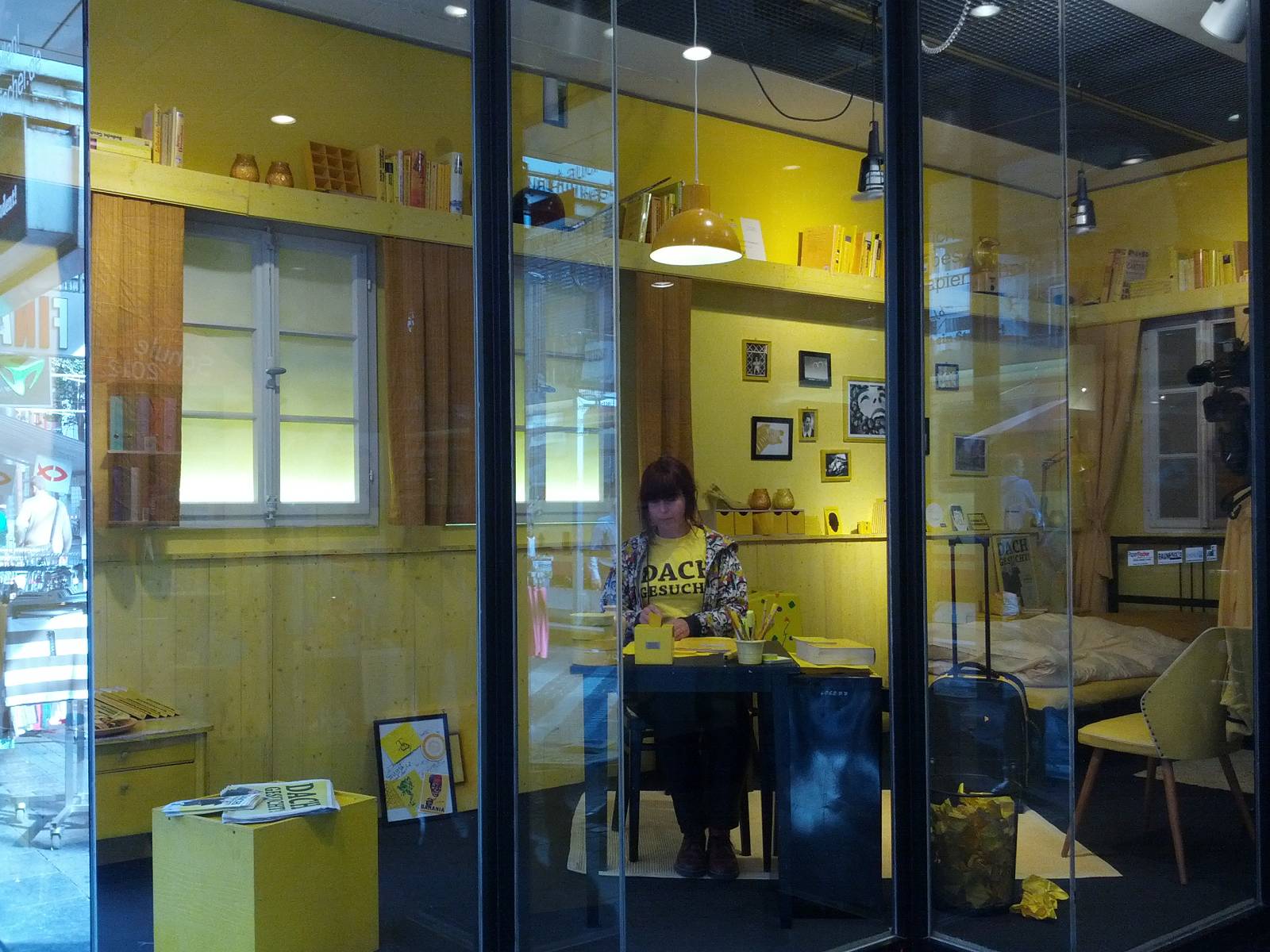Studentin sitzt an einem Schreibtisch eines volleingerichteten Zimmers, das in einem Schaufenster steht