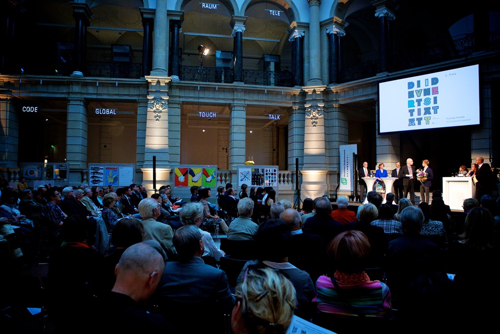 Der gut gefüllte Lichthof des Museums für Kommunikation während der Preisverleihung, auf der Bühne der 2.Preis-Träger Thomas Stralek.
