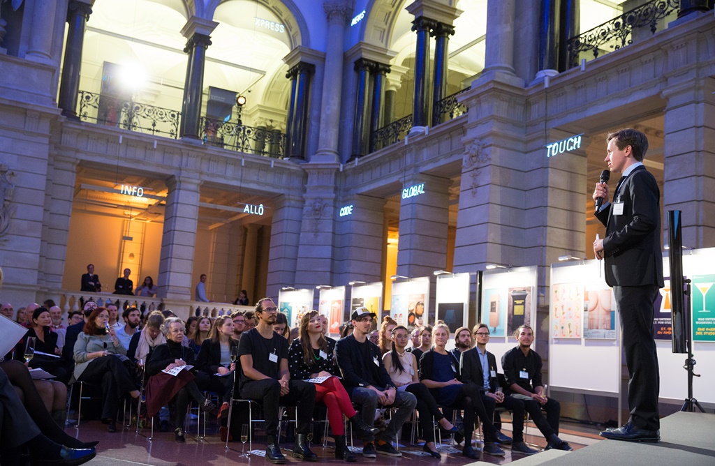 Auf dem Bild ist das gesamte Publikum im Lichthof des Museums für Kommunikation zu sehen, auf der Bühne steht der Moderator.