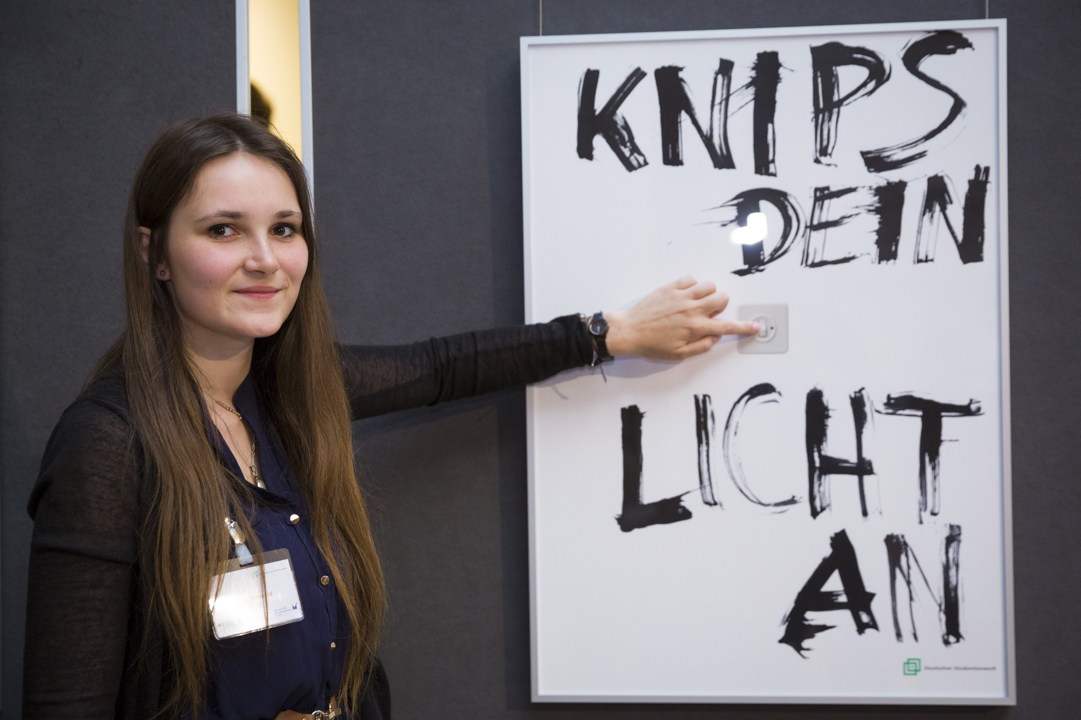 Eine junge Frau neben dem erstplatzierten Plakat mit dem Schriftzug "Knips dein Licht an"